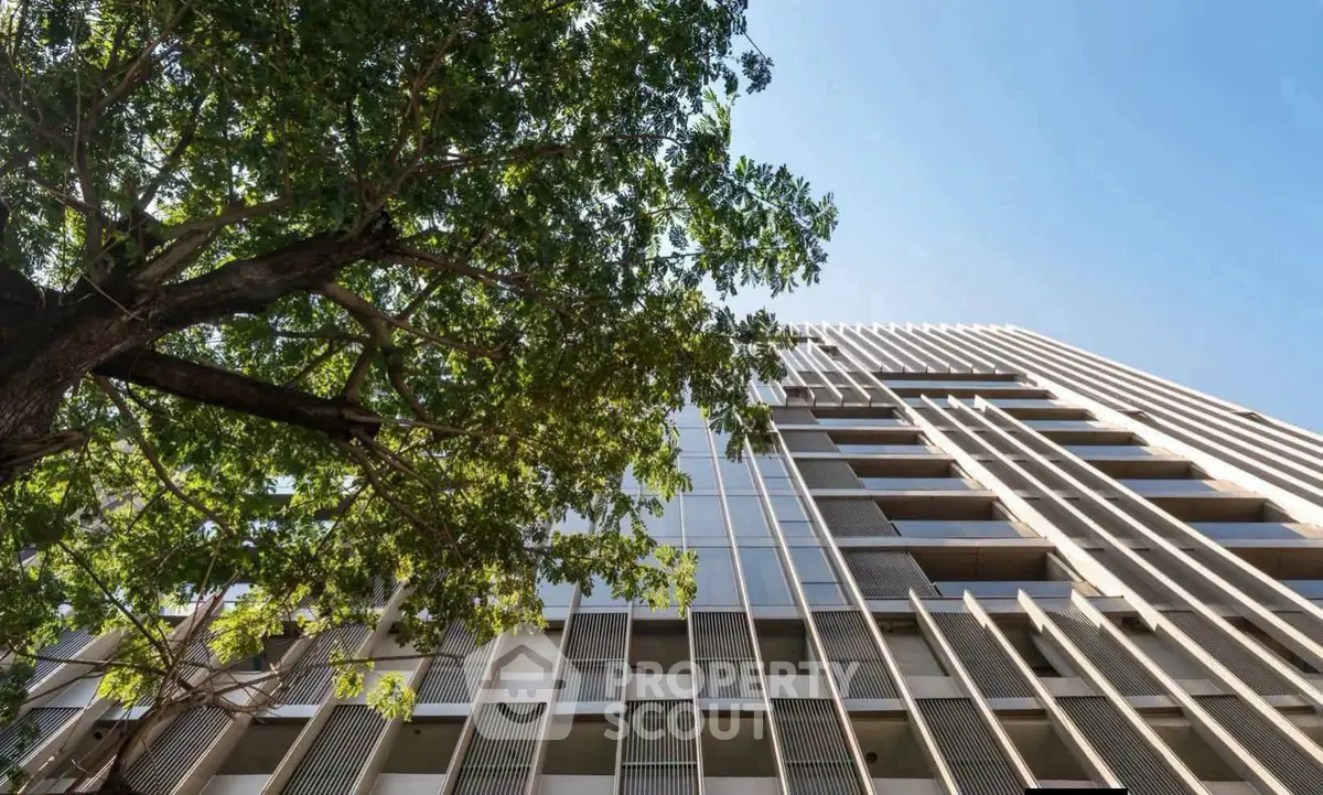 Modern high-rise building with sleek architectural design and lush tree in foreground.