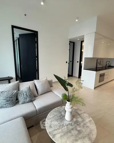 Modern living room with sleek design and open kitchen layout, featuring stylish furniture and decor.
