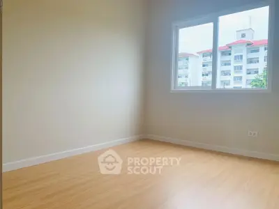 Bright empty room with wooden flooring and large window view.