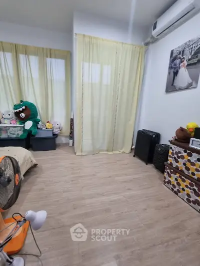 Cozy bedroom with wooden flooring and soft yellow curtains, featuring plush toys and modern decor.