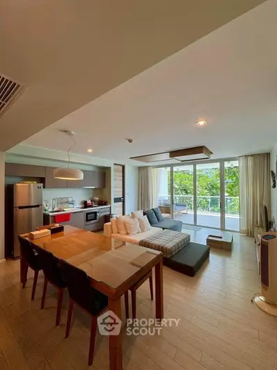 Spacious open-plan living room with modern kitchen and large windows overlooking greenery.
