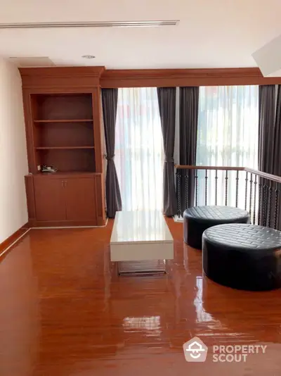 Elegant living space with polished hardwood floors, custom built-in shelving, and expansive windows draped in luxurious curtains.