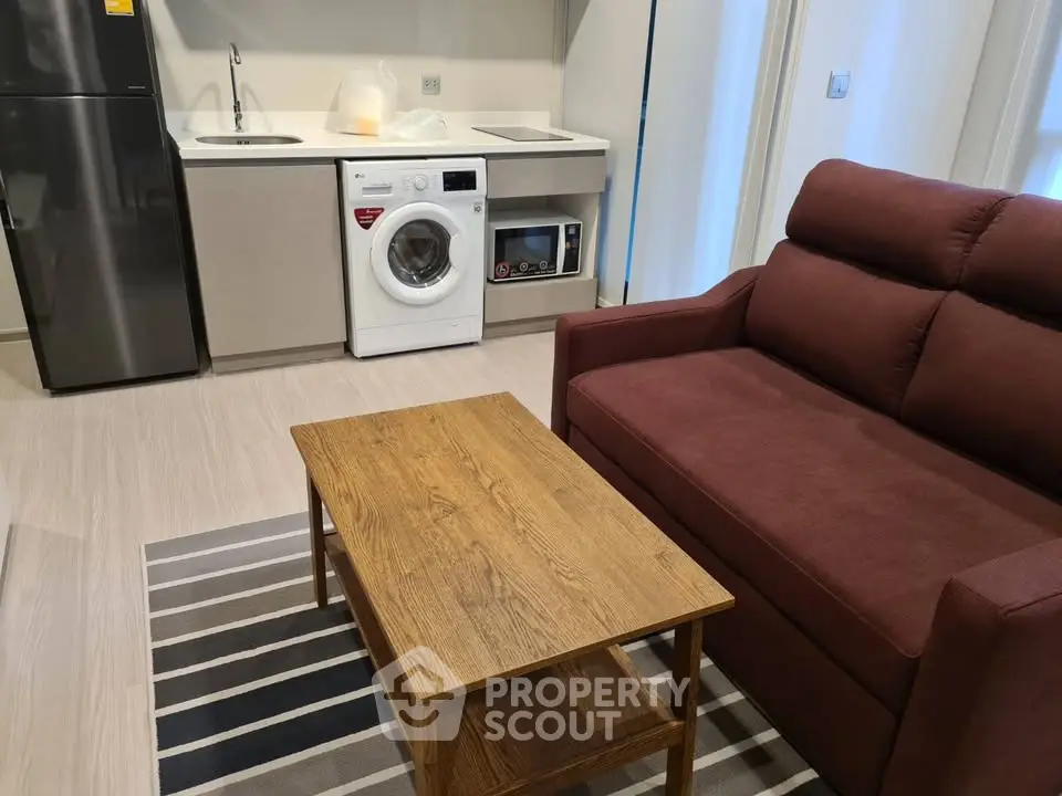 Modern living room with compact kitchen featuring washing machine and stylish furniture.