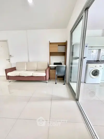 Modern living room with sleek sofa and adjacent laundry area featuring washing machine.