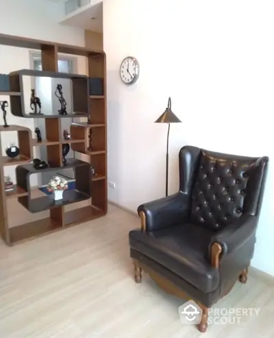 Elegant living space featuring a classic leather armchair and a stylish wooden bookshelf, complemented by a chic floor lamp and a minimalist wall clock.