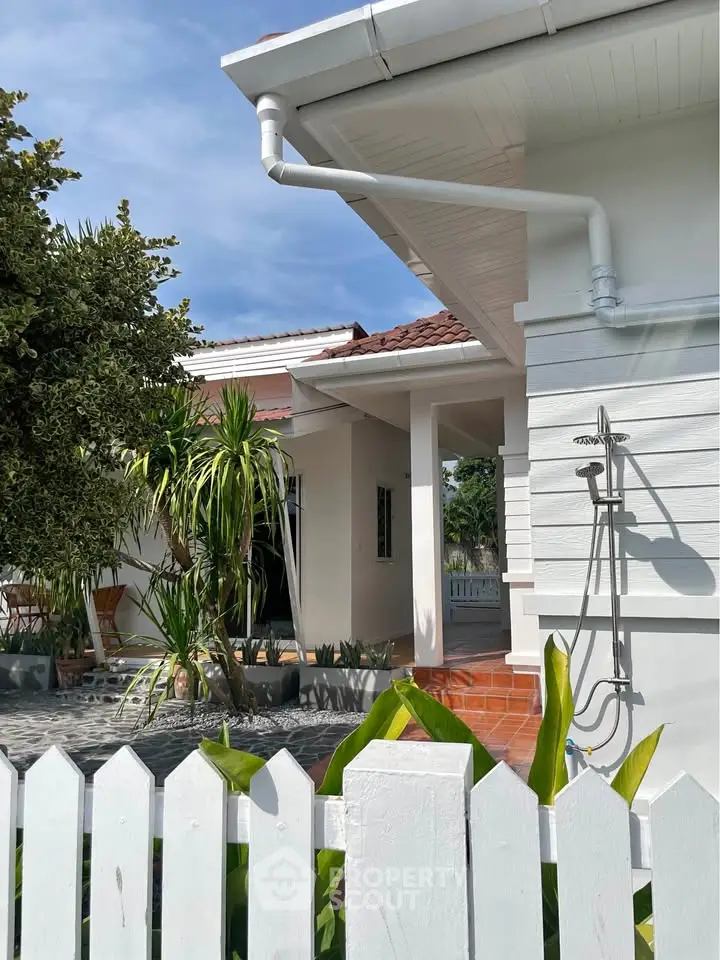 Charming white house with outdoor shower and lush greenery, perfect for tropical living.