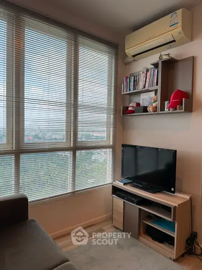 Cozy living room with large windows and air conditioning, featuring a TV and bookshelf.