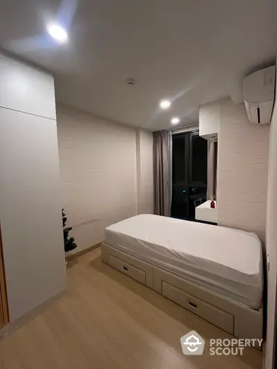 Modern minimalist bedroom with single bed and built-in storage, featuring sleek design and natural light.