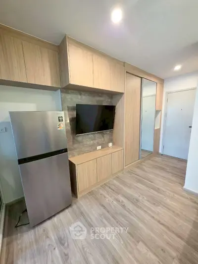 Modern kitchen with sleek cabinetry and stainless steel fridge in compact apartment.