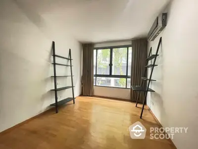 Spacious study room with wooden flooring, large window, and modern shelving units, perfect for a home office setup.