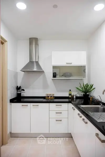 Modern kitchen with sleek white cabinets and black countertops, featuring a stainless steel range hood and sink.
