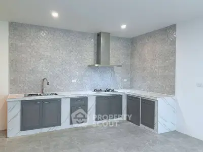 Modern kitchen with sleek gray cabinets and marble countertops, featuring a gas stove and stylish backsplash.