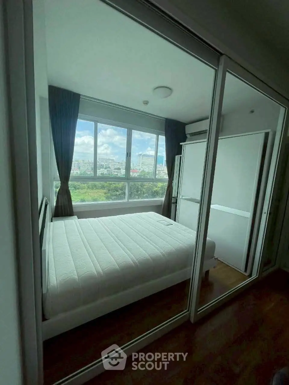Modern bedroom with large window and mirrored closet doors, offering a bright and airy atmosphere.