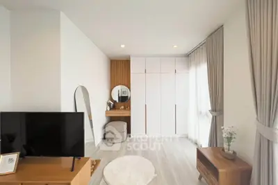 Modern living room with sleek furniture and natural light, featuring a TV and stylish decor.