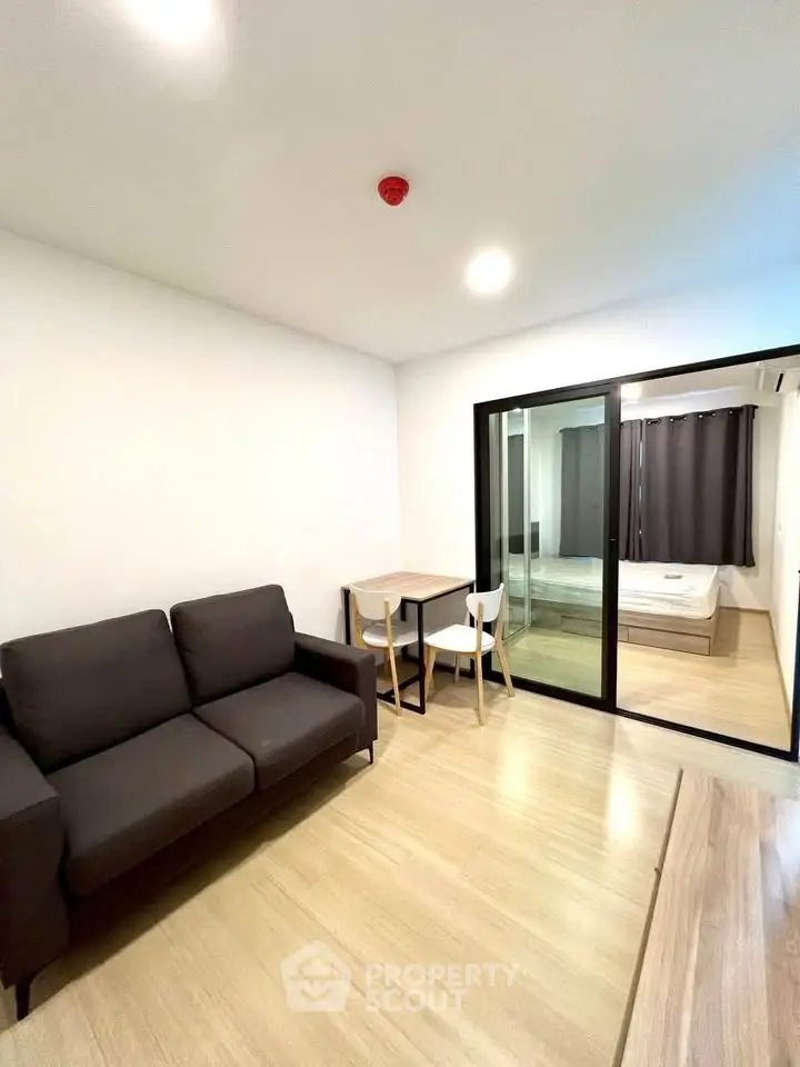 Modern apartment interior with cozy living room and bedroom view, featuring sleek furniture and wooden flooring.