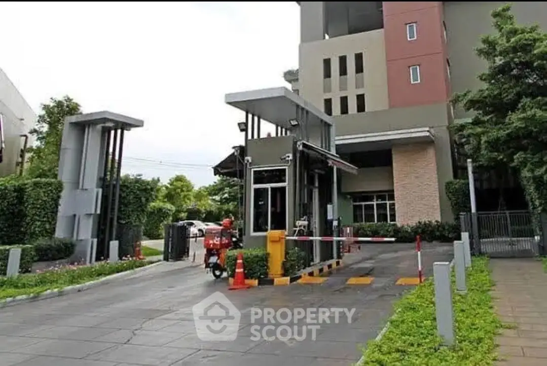 Modern gated entrance of residential building with security booth and lush greenery.