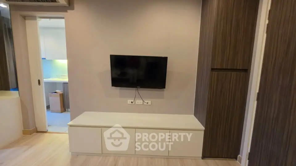 Modern living room with wall-mounted TV and sleek storage unit, adjacent to a contemporary kitchen.
