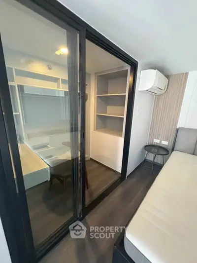Modern bedroom with sliding glass doors and built-in shelves, featuring sleek design and air conditioning.