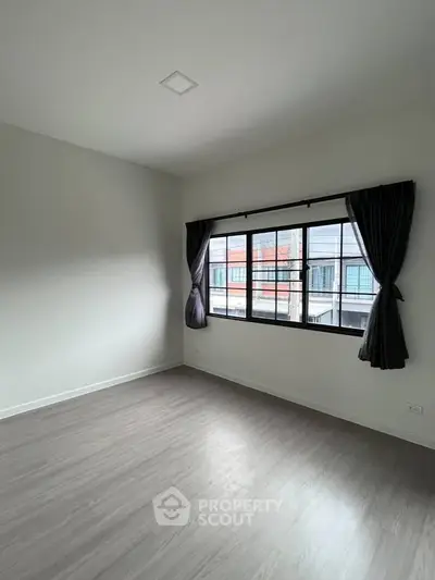 Spacious empty room with large window and modern flooring, perfect for customization.