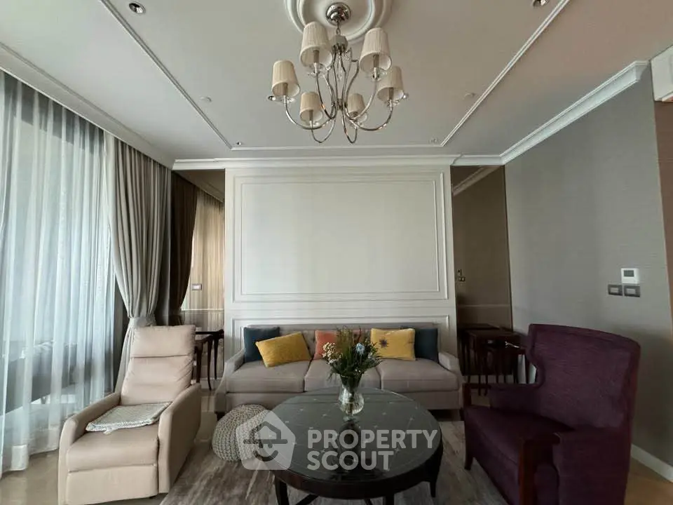 Elegant living room with stylish furniture and chandelier, featuring a cozy seating area and large windows.