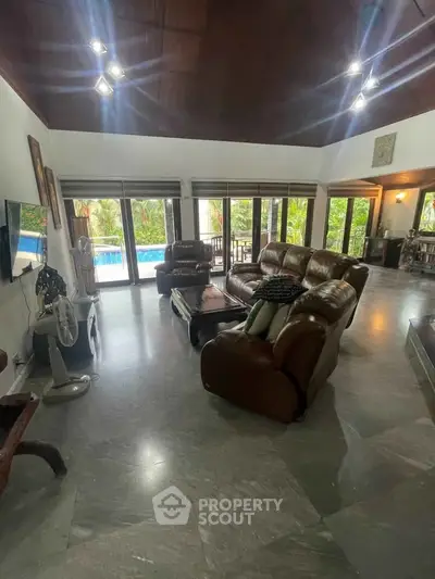 Spacious living room with leather sofas and pool view, perfect for relaxation and entertainment.