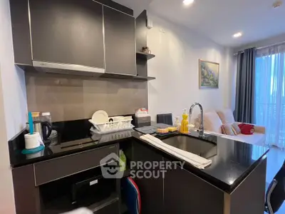 Modern kitchen with sleek black countertops and cozy living area in open layout apartment.