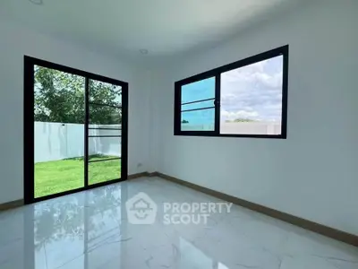 Bright and airy room with large windows overlooking a lush garden, perfect for relaxation and natural light.