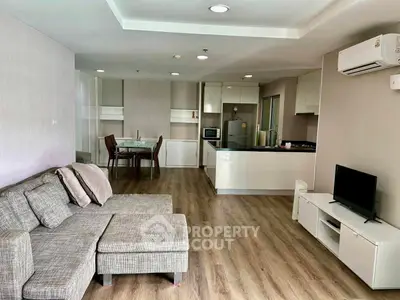 Spacious open-plan living room with modern kitchen and dining area, featuring sleek furniture and wooden flooring.