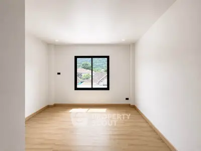 Spacious empty room with wooden flooring and large window offering scenic view.