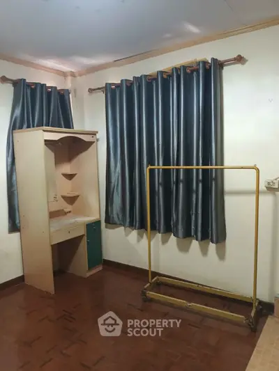 Cozy bedroom with wooden flooring and elegant curtains, featuring a compact desk and clothes rack.