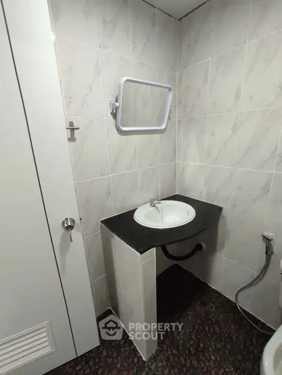 Compact bathroom with modern sink and wall-mounted mirror, featuring sleek tile design.