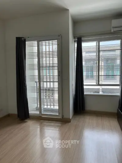 Bright room with large windows and wooden flooring, perfect for a cozy living space.