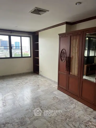 Spacious room with large window and wooden wardrobe, offering city views.