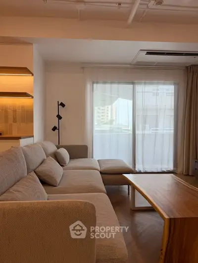 Modern living room with cozy sectional sofa and wooden coffee table, featuring large window with city view.
