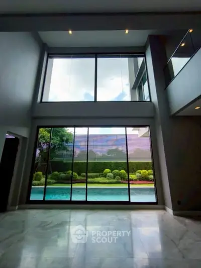 Luxurious modern living room with floor-to-ceiling windows overlooking a serene pool and garden.