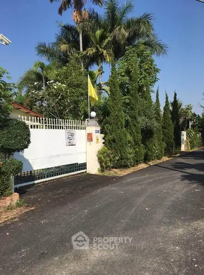 Charming gated entrance with lush greenery and tall trees lining the driveway.