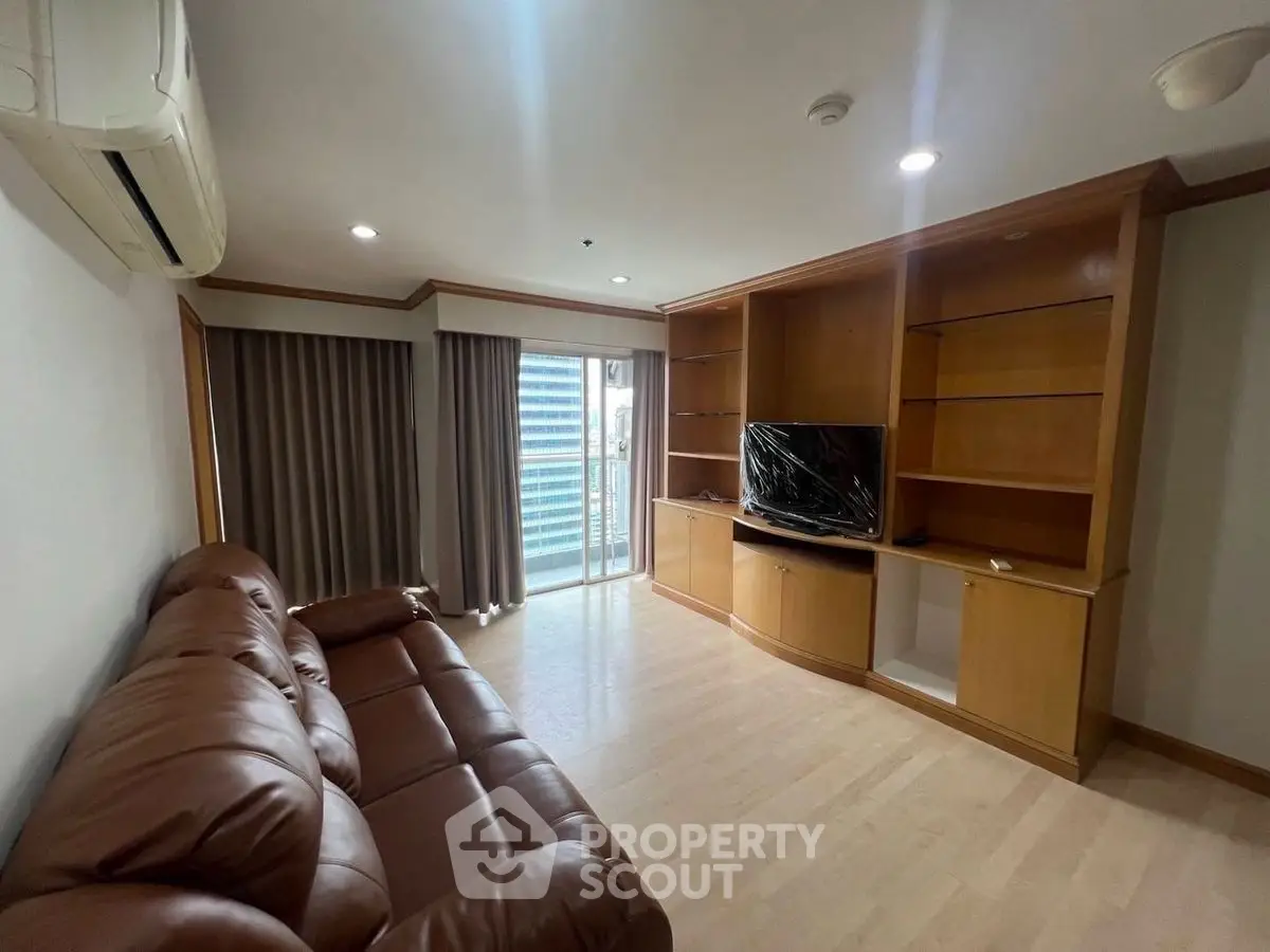 Spacious living room with leather sofa and built-in wooden shelves, featuring a city view balcony.