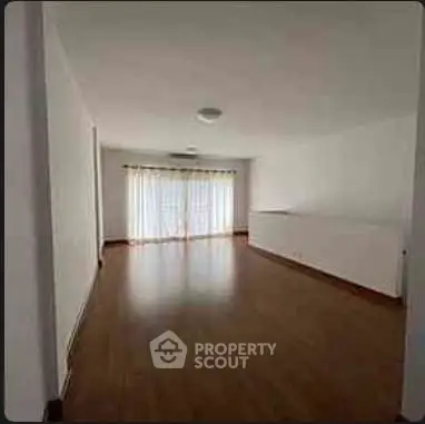 Spacious empty living room with wooden flooring and large window.