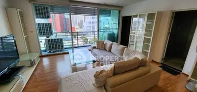 Spacious living room with large windows and city view, featuring modern furniture and wooden flooring.