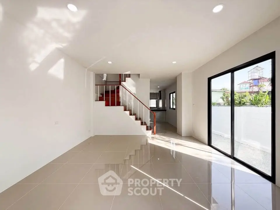 Spacious modern living room with sleek staircase and large windows offering abundant natural light.