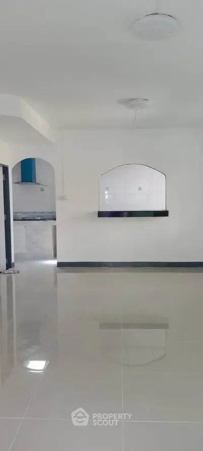 Spacious open-plan living area with glossy tiled floors and arched kitchen pass-through.