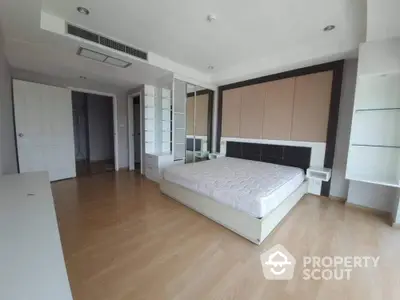 Spacious bedroom with large bed, mirrored wardrobe, and hardwood floors in a modern apartment, offering a blend of comfort and elegance.