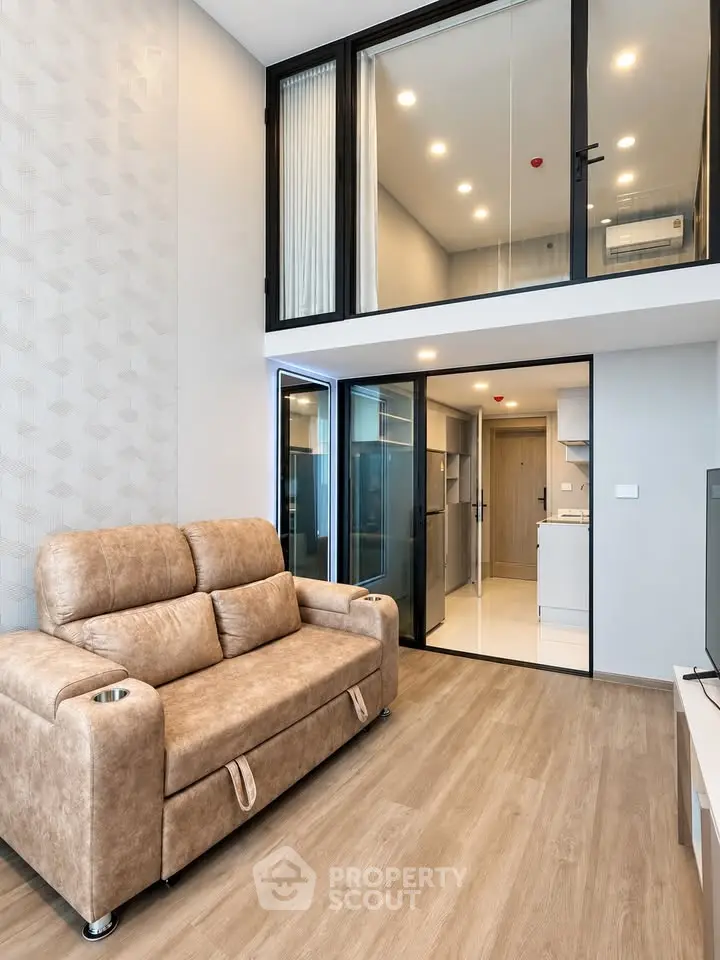 Modern loft-style living room with high ceiling and mezzanine, featuring sleek furniture and open kitchen layout.