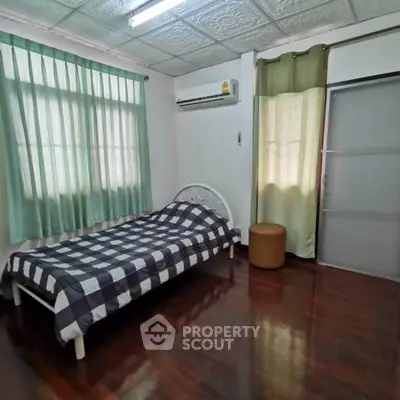 Cozy bedroom with wooden flooring and natural light, featuring a single bed and air conditioning.