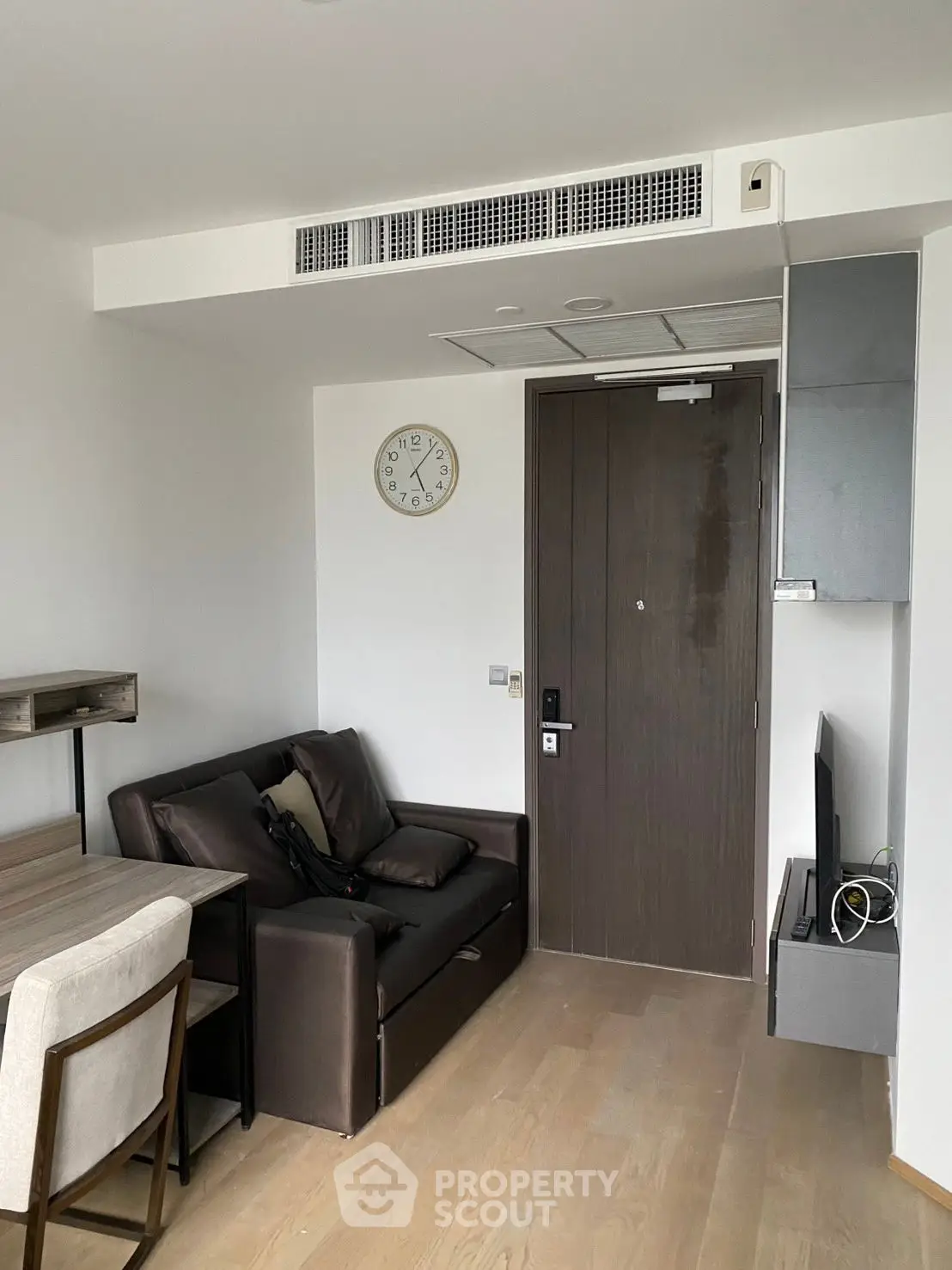 Modern living room with sleek furniture and wall clock, featuring wooden flooring and neutral tones.
