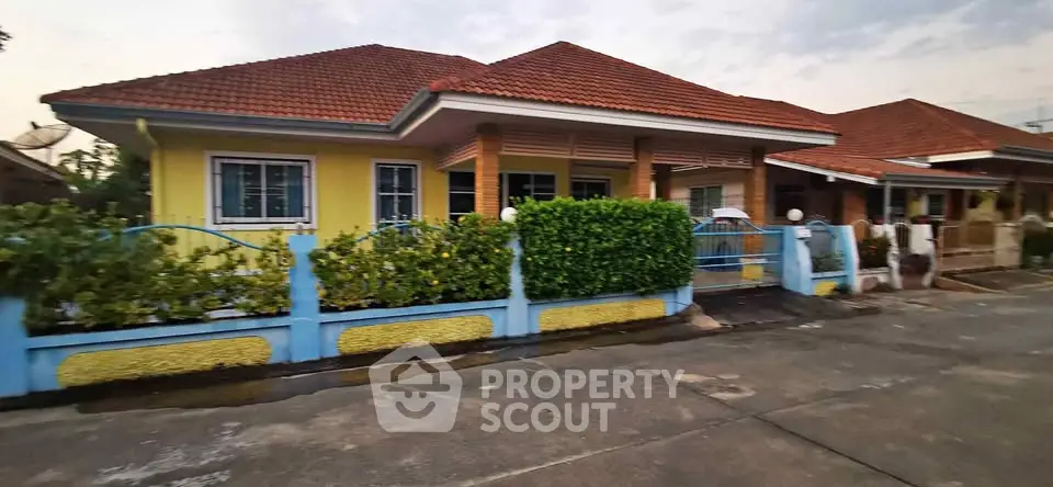 Charming single-story home with vibrant yellow facade and red-tiled roof, surrounded by lush greenery.