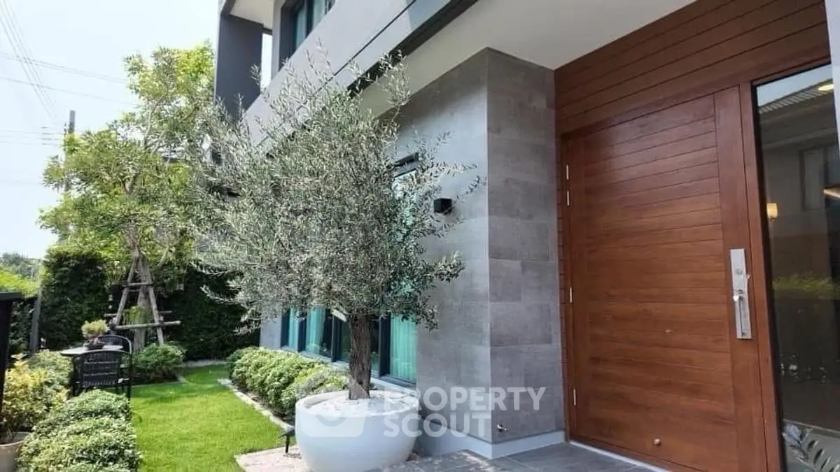 Modern home entrance with wooden door and lush garden landscaping.