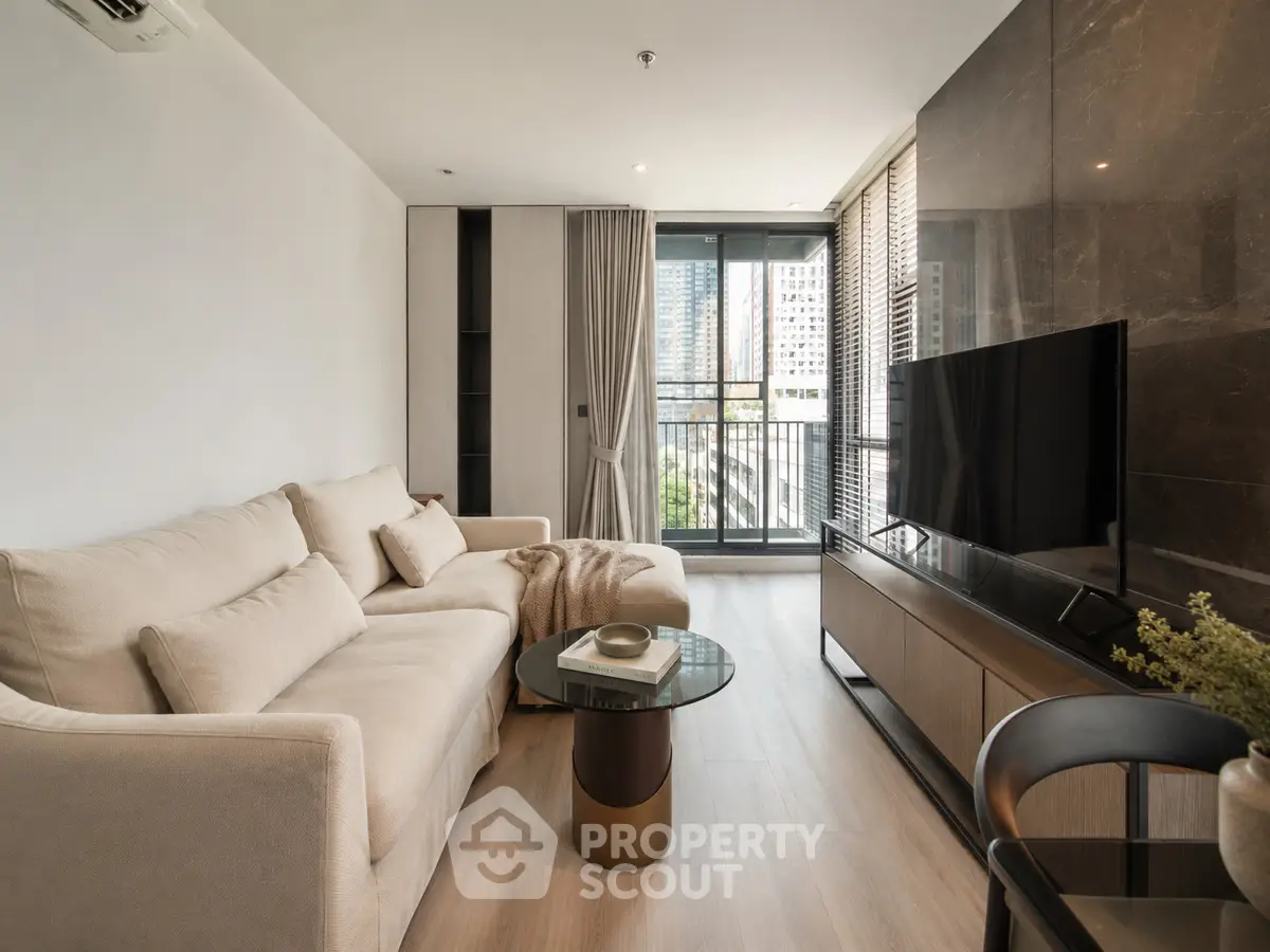 Modern living room with elegant decor and city view balcony, featuring a cozy beige sofa and sleek TV setup.