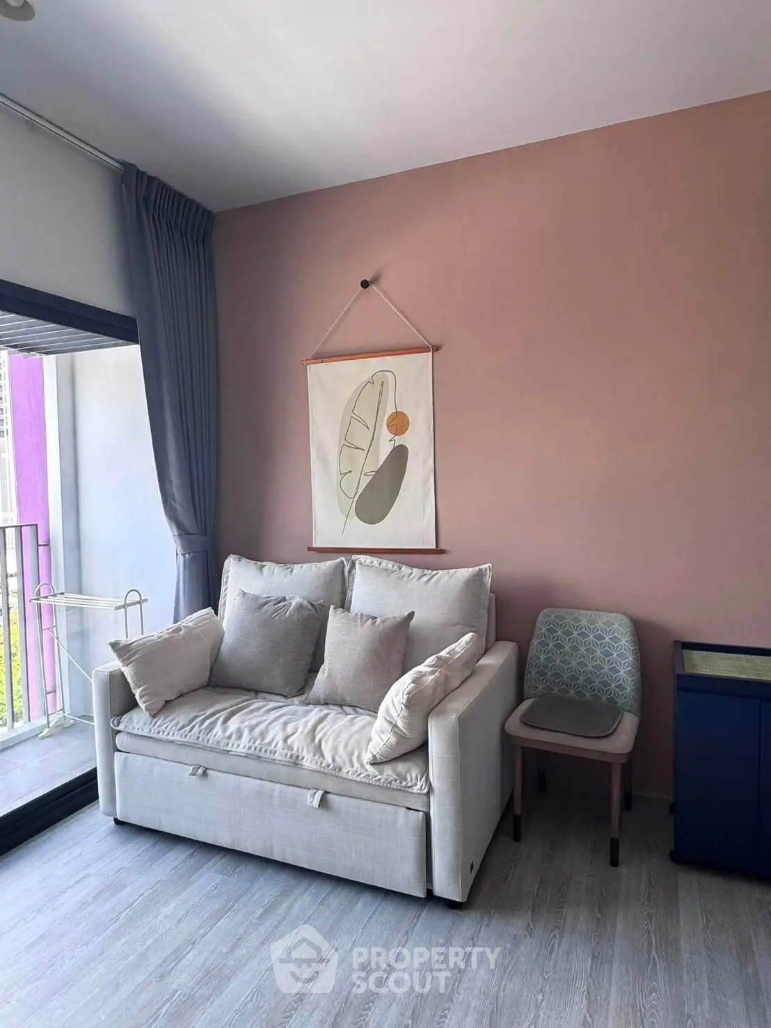 Cozy living room with modern decor and balcony access, featuring a stylish sofa and artistic wall hanging.