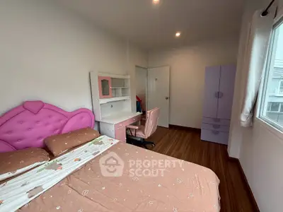 Charming bedroom with pink accents and wooden flooring, featuring a cozy bed and study desk by the window.